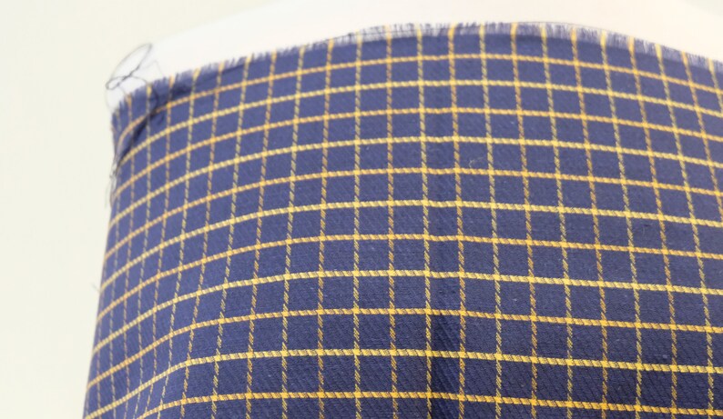 May include: A close-up of a navy blue fabric with a yellow checkered pattern.