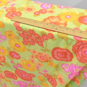 Puede incluir: Una tela verde con estampado floral con grandes flores naranjas, amarillas y rosas. La tela se muestra con una regla para la escala.