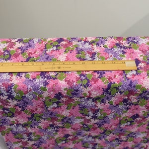 May include: A close-up of a fabric with a floral print. The fabric is a mix of pink, purple, and green. The flowers are small and clustered together. A ruler is placed on top of the fabric to show the scale.