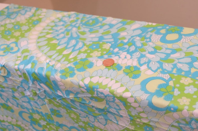 May include: A close-up of a fabric with a swirling pattern in shades of blue, green, and white. The fabric has a paisley-like design.