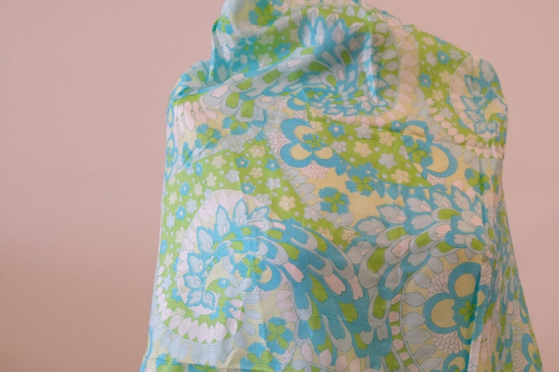 May include: A blue and green paisley patterned fabric with white accents. The fabric is draped over a surface.