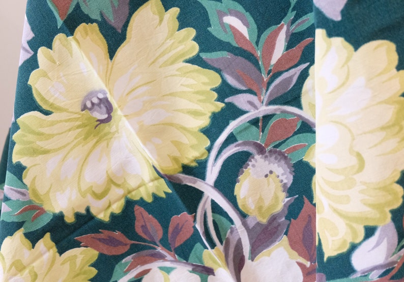 K&ouml;nnte beinhalten: Nahaufnahme eines Stoffes mit Blumenmuster. Der Stoff ist gr&uuml;n mit gelben, wei&szlig;en und braunen Blumen. Die Blumen sind stilisiert und haben einen Vintage-Look.