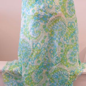 May include: A light blue and green fabric with a swirling floral pattern. The fabric is draped over a form and has a white background.