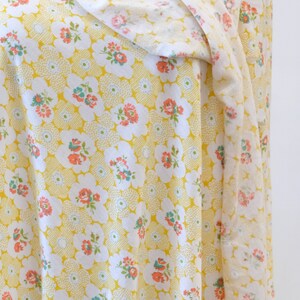 Puede incluir: Tela amarilla con un patr&oacute;n floral blanco. La tela tiene un peque&ntilde;o patr&oacute;n repetitivo de flores blancas con centros rosados y hojas verdes. La tela est&aacute; doblada de una manera que muestra el patr&oacute;n desde diferentes &aacute;ngulos.