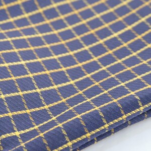 May include: A folded blue and yellow checkered kitchen towel. The towel is made of a soft, textured fabric.