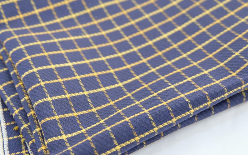 May include: A folded blue and yellow checkered kitchen towel. The towel is made of a soft, textured fabric.