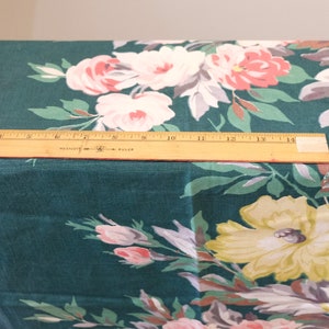 K&ouml;nnte beinhalten: Nahaufnahme eines t&uuml;rkisfarbenen Stoffes mit einem Blumendruck mit gro&szlig;en rosa, wei&szlig;en und gelben Bl&uuml;ten. Ein Holzliniall liegt auf dem Stoff.