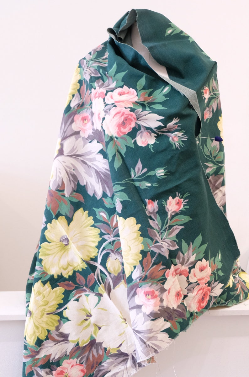K&ouml;nnte beinhalten: Ein gr&uuml;ner Stoff mit einem Blumendruck mit rosa, wei&szlig;en und gelben Blumen. Der Stoff hat einen Vintage-Charakter und w&auml;re perfekt f&uuml;r Bastel- oder N&auml;hprojekte.