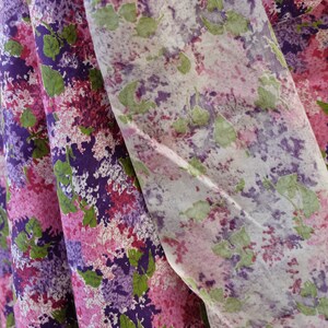 May include: A close-up of a fabric with a pink, purple and green floral pattern. The fabric is folded in half, and the pattern is visible on both sides.