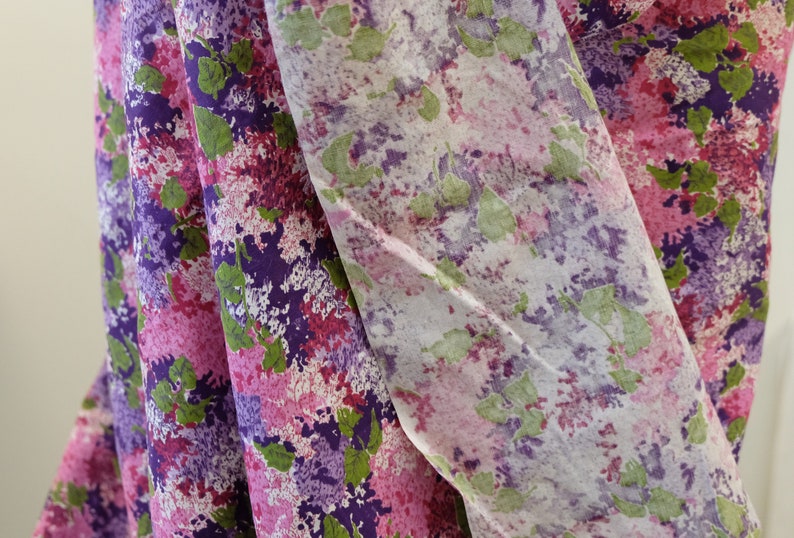 May include: A close-up of a fabric with a pink, purple and green floral pattern. The fabric is folded in half, and the pattern is visible on both sides.
