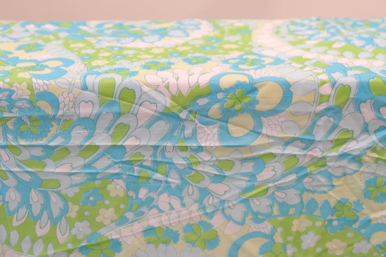 May include: A blue and green fabric with a floral pattern. The fabric has a light blue background with green and white flowers.