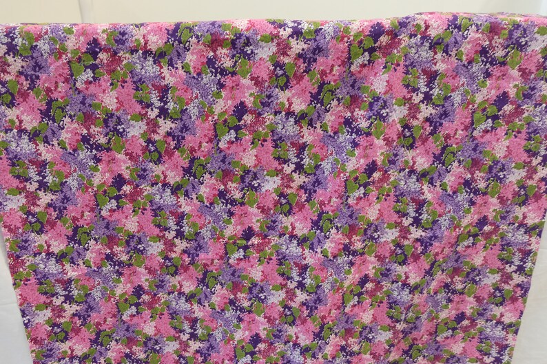May include: A pink and purple floral fabric with a small-scale print. The fabric features a repeating pattern of pink, purple, and green flowers.