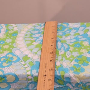 May include: A wooden ruler with inch markings is placed on top of a fabric with a blue, green, and white floral pattern.