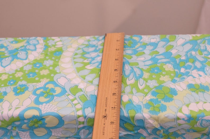 May include: A wooden ruler with inch markings is placed on top of a fabric with a blue, green, and white floral pattern.