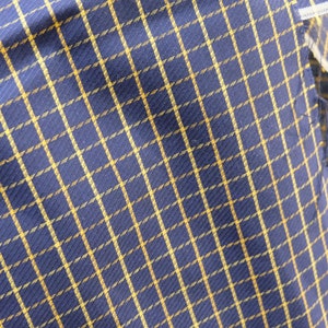 May include: A close-up of a blue and gold plaid fabric. The fabric has a woven texture and a subtle sheen.