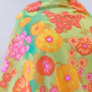 Puede incluir: Una tela verde con un patr&oacute;n floral que presenta grandes flores naranjas, amarillas y rosas. El fondo es de color verde claro.