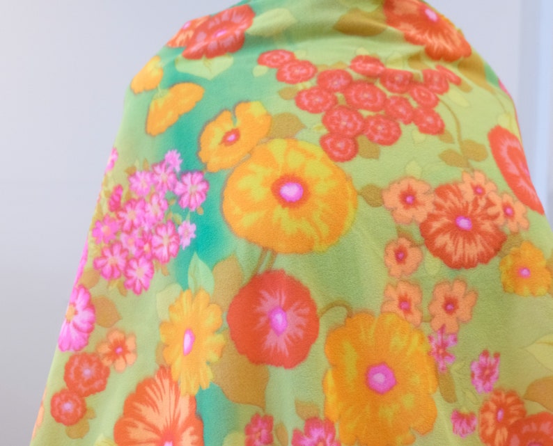 Puede incluir: Una tela verde con un patr&oacute;n floral que presenta grandes flores naranjas, amarillas y rosas. El fondo es de color verde claro.