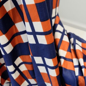 May include: Close-up of a fabric with a geometric pattern in shades of orange, white, and blue. The fabric is folded and the pattern is visible in the folds.