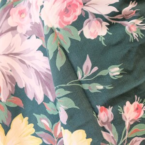 K&ouml;nnte beinhalten: Gr&uuml;ner Stoff mit einem floralen Muster mit rosa, wei&szlig;en und gelben Blumen. Der Stoff hat eine strukturierte Oberfl&auml;che.