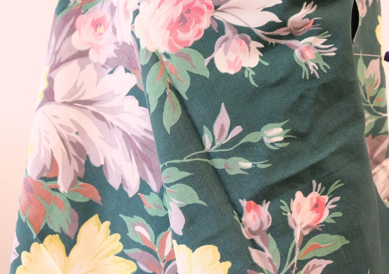 K&ouml;nnte beinhalten: Gr&uuml;ner Stoff mit einem floralen Muster mit rosa, wei&szlig;en und gelben Blumen. Der Stoff hat eine strukturierte Oberfl&auml;che.
