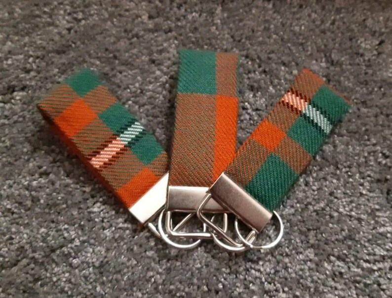 Puede incluir: Tres llaveros con tela de cuadros naranja, verde y marr&oacute;n. Cada llavero tiene un anillo de metal plateado y un cierre de metal plateado.