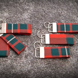 Puede incluir: Cinco llaveros de tela con estampado de cuadros rojos, verdes y blancos con anillas de plata.