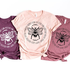 May include: Three t-shirts with a bee graphic and the text "BE YOURSELF - HUMBLE - KIND - POSITIVE - FUN - CONFIDENT - BRAVE - SMART - HAPPY - WILD - CREATIVE - JOYFUL" around the bee.
