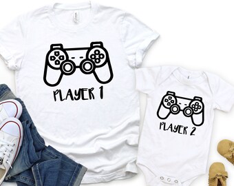 May include: Two white t-shirts with a black gamepad graphic and the text "Player 1" and "Player 2".