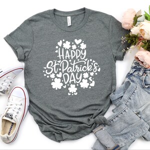 May include: A heather grey t-shirt with a white graphic that says "Happy St. Patrick's Day" surrounded by shamrocks and hearts.
