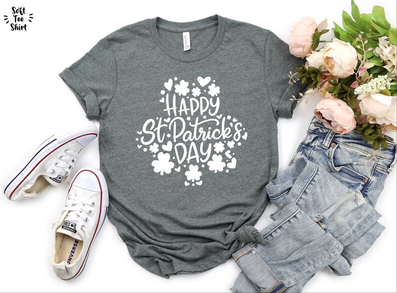 May include: A heather grey t-shirt with a white graphic that says "Happy St. Patrick's Day" surrounded by shamrocks and hearts.