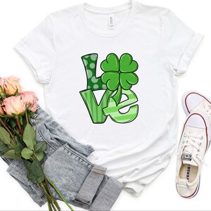 May include: White t-shirt with a green "LOVE" graphic featuring a four-leaf clover.