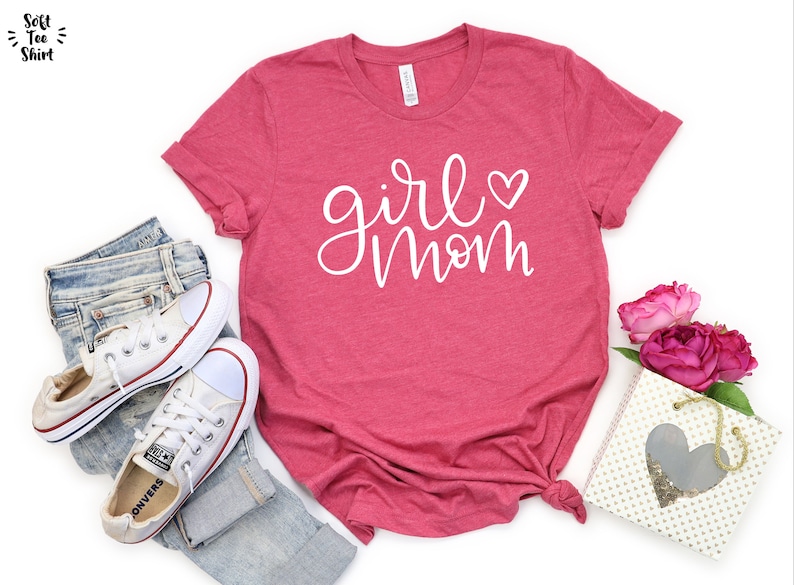 May include: A pink t-shirt with the text "girl mom" in white script with a small heart next to the word "girl".