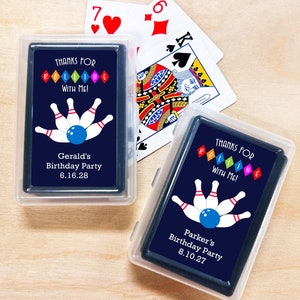 May include: Two clear plastic boxes containing decks of playing cards with custom designs. The cards feature a bowling theme with the text "Thanks for Rolling with Me!" and personalized birthday party details. The top box has the text "Gerald's Birthday Party 6.16.28" and the bottom box has the text "Parker's Birthday Party 8.10.27".