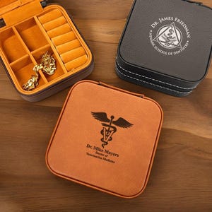 May include: Two brown leather jewelry boxes with different engravings. One box has a medical symbol and the text "Dr. Mike Mayers, Doctor of Veterinarian Medicine". The other box has a dental symbol and the text "Dr. James Friedman, Newark School of Dentistry".