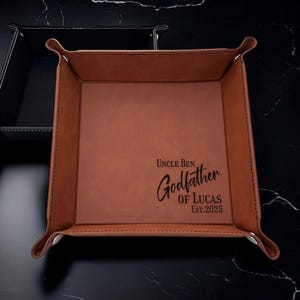 May include: A brown leather valet tray with the text "Uncle Ben Godfather of Lucas Est. 2023" engraved on it.