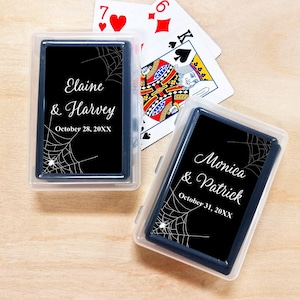 May include: Two clear plastic cases containing decks of playing cards with black labels featuring white spider web designs and small spiders. One label reads Elaine & Harvey October 28, 20XX, and the other reads Monica & Patrick October 31, 20XX.
