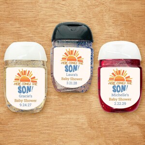 May include: Three clear plastic bottles of hand sanitizer with colorful labels that say "Here comes the son!" with a sunset graphic and a date. The labels are personalized with different names and dates.