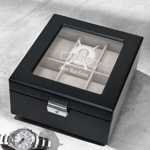 May include: Black wooden watch box with a glass top. The box has eight compartments for storing watches. The box is engraved with the text "Richard Best Dad Ever" and a pool ball with crossed pool cues.