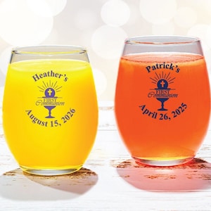May include: Two clear glass wine glasses with personalized text for a First Communion celebration. The glass on the left has yellow liquid and says "Heather's First Communion August 15, 2026". The glass on the right has orange liquid and says "Patrick's First Communion April 26, 2025".