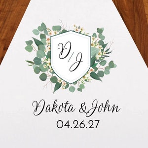 May include: White wedding aisle runner with a green and white floral design. The design features a shield with the initials "D/J" and the text "Dakota & John 04.26.27".