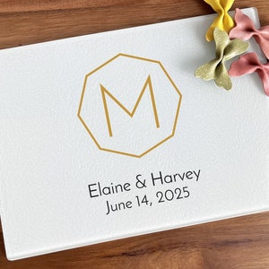 May include: White glass cutting board with a gold geometric monogram "M" and the text "Elaine & Harvey June 14, 2025".