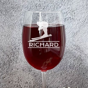May include: A clear wine glass with a red wine inside. The glass is engraved with a skier and the name "RICHARD".