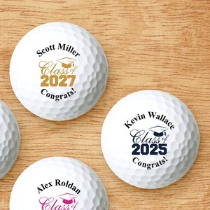 May include: Four white golf balls with personalized graduation messages. Each ball features a different name, graduation year, and color scheme. The names are Katie Friedman, Scott Miller, Alex Roldan, and Kevin Wallace.
