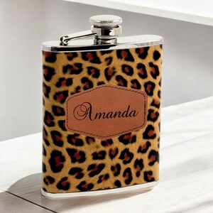 May include: A stainless steel flask with a leopard print design and a brown leather patch with the name "Amanda" engraved on it.