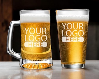 May include: Two clear glass beer mugs with handles. The mug on the left is a traditional beer stein with a wide base. The mug on the right is a tall, slender pint glass. Both mugs are filled with a golden yellow beer and have the text "YOUR LOGO HERE" etched on the side.