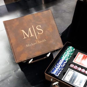 May include: A brown leatherette poker set with the initials "MS" and the name "Michael Smith" engraved on the lid. The open case reveals poker chips, playing cards, and dice.