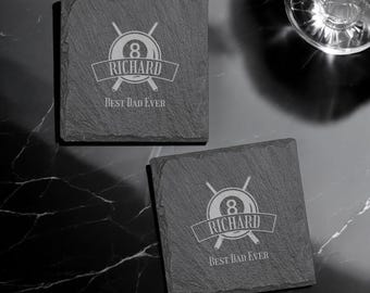 May include: Two black slate coasters with a white design of crossed pool cues and a billiard ball with the number 8. The text "Richard Best Dad Ever" is on each coaster.
