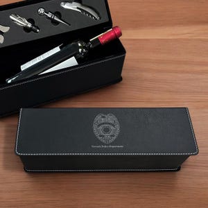 May include: Black leather gift box with a wine bottle and accessories inside. The box is engraved with a police badge and the text "Newark Police Department".