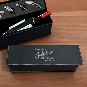 May include: A black leatherette wine gift set with a bottle of wine and wine tools. The set includes a corkscrew, bottle stopper, and other accessories. The box is personalized with the text "Uncle Ben Godfather of Lucas Est. 2025".