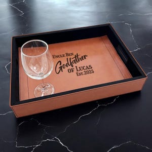 May include: A brown leather serving tray with a black border and a glass. The tray is engraved with the text "Uncle Ben Godfather of Lucas Est. 2025".